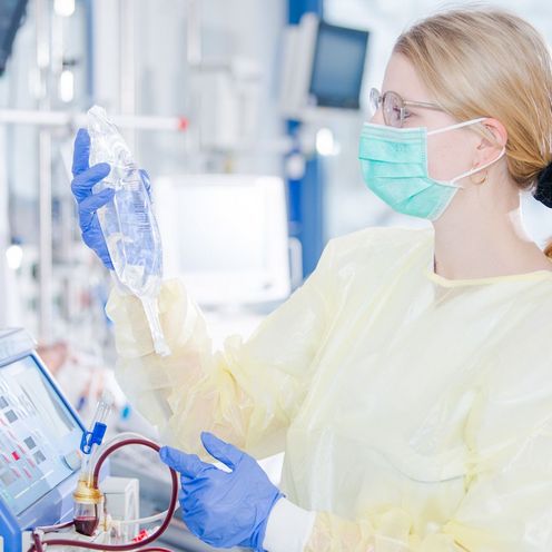 Eine Krankenpflegerin in Schutzkleidung und Mundschutz begutachtet eine Infusion im Zimmer einer Intensivstation im Krankenhaus.