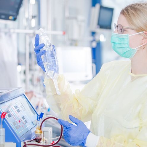 Eine Krankenpflegerin in Schutzkleidung und Mundschutz begutachtet eine Infusion im Zimmer einer Intensivstation im Krankenhaus.