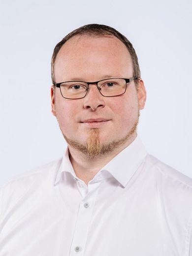 Auf dem Bild ist Christian Dierken zusehen. Er hat kurzes dunkelblondes Haar und einen Bart. Er trägt eine Brille und ein weißes Hemd.