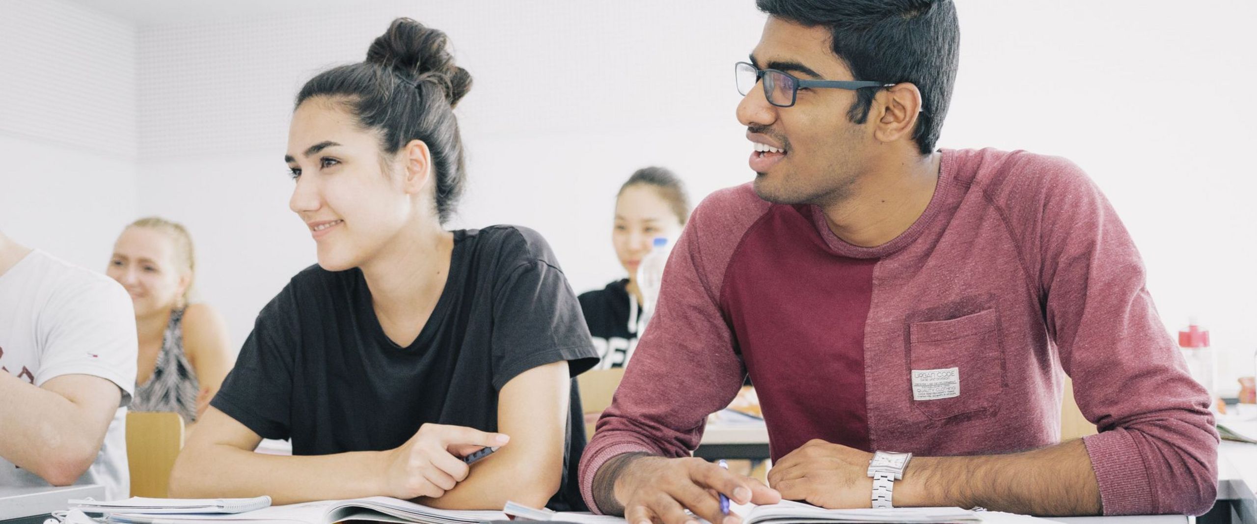 Studierende sitzen nebeneinander an Tischen in einem Seminarraum.