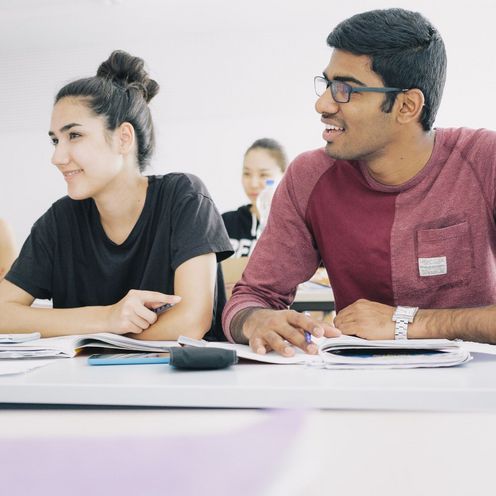 Studierende sitzen nebeneinander an Tischen in einem Seminarraum.