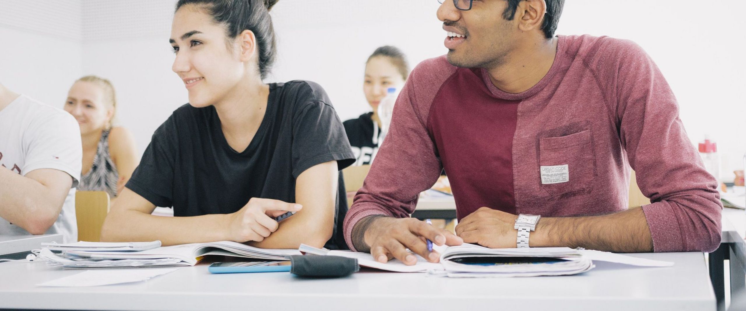 Studierende sitzen nebeneinander an Tischen in einem Seminarraum.