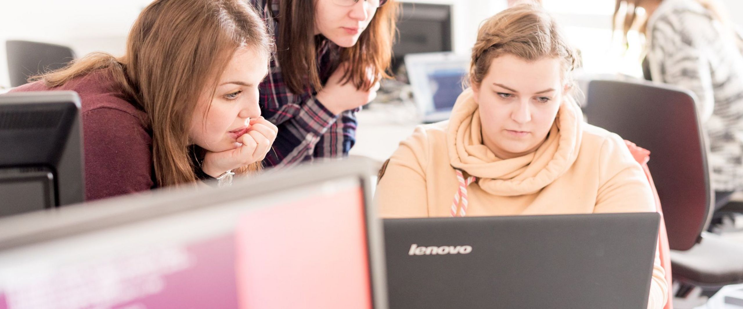 Drei Studentinnen programmieren am Laptop. 