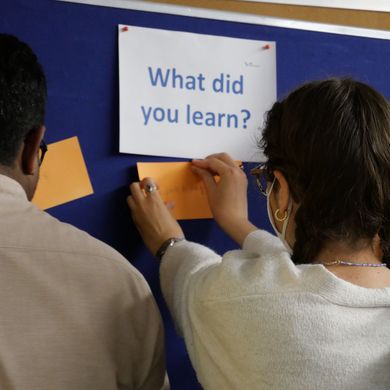 Tausche Erfahrungen aus Studierende heften Notizzettel an Aufstellwand mit Aufschrift: What did you learn?