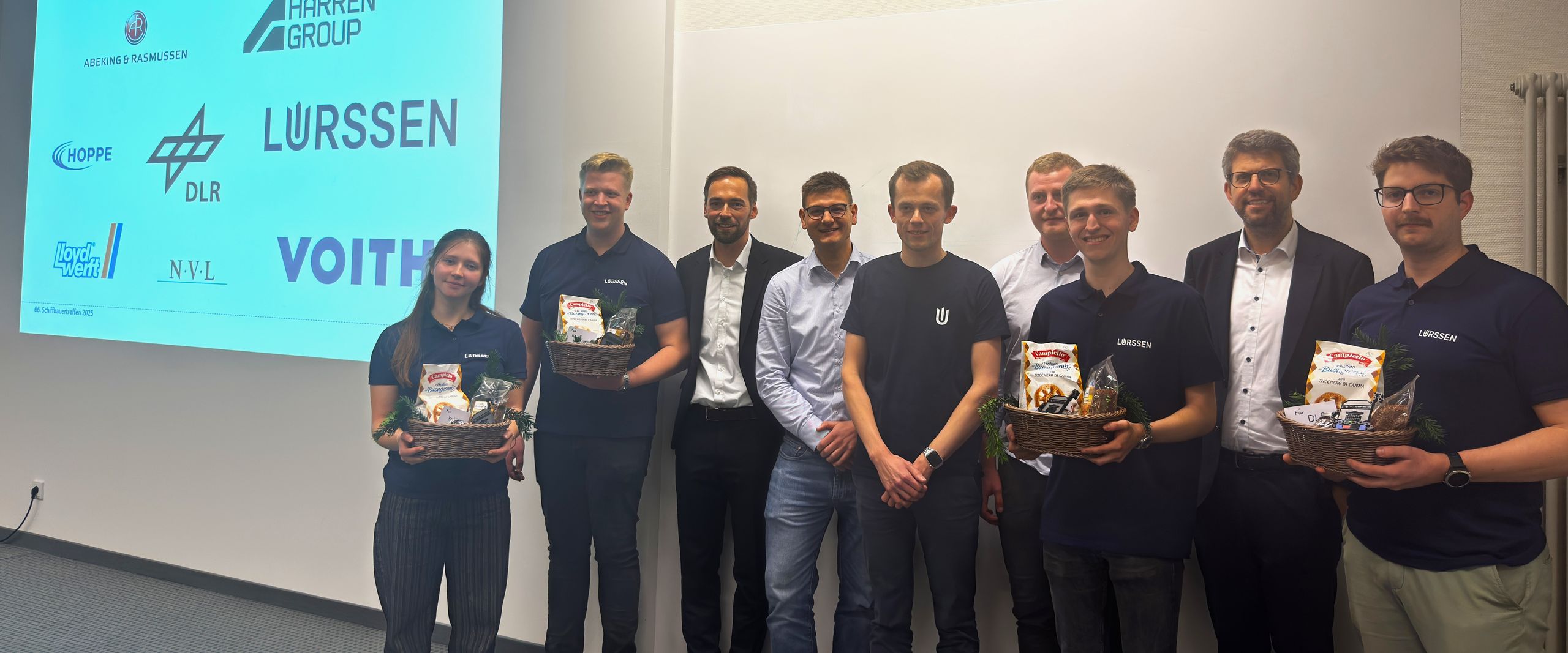 202511 66. Schiffbauertreffen Gruppenbild mit Männern und Frauen vor einer Power-Point-Präsentation