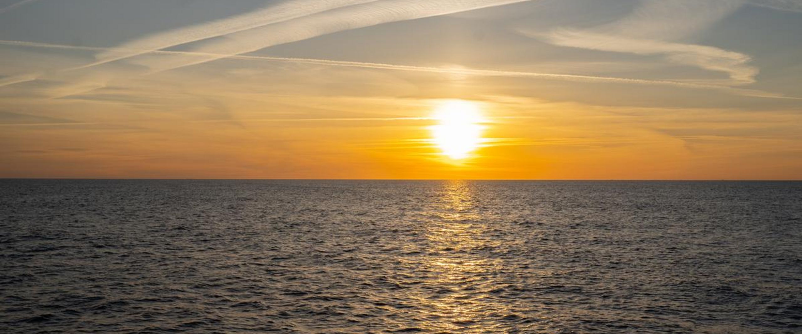 Nordsee Sonne Sonne steht hinter einem gelben Himmel über dem Horizont. Im Vordergrund ist das Meer zu sehen.