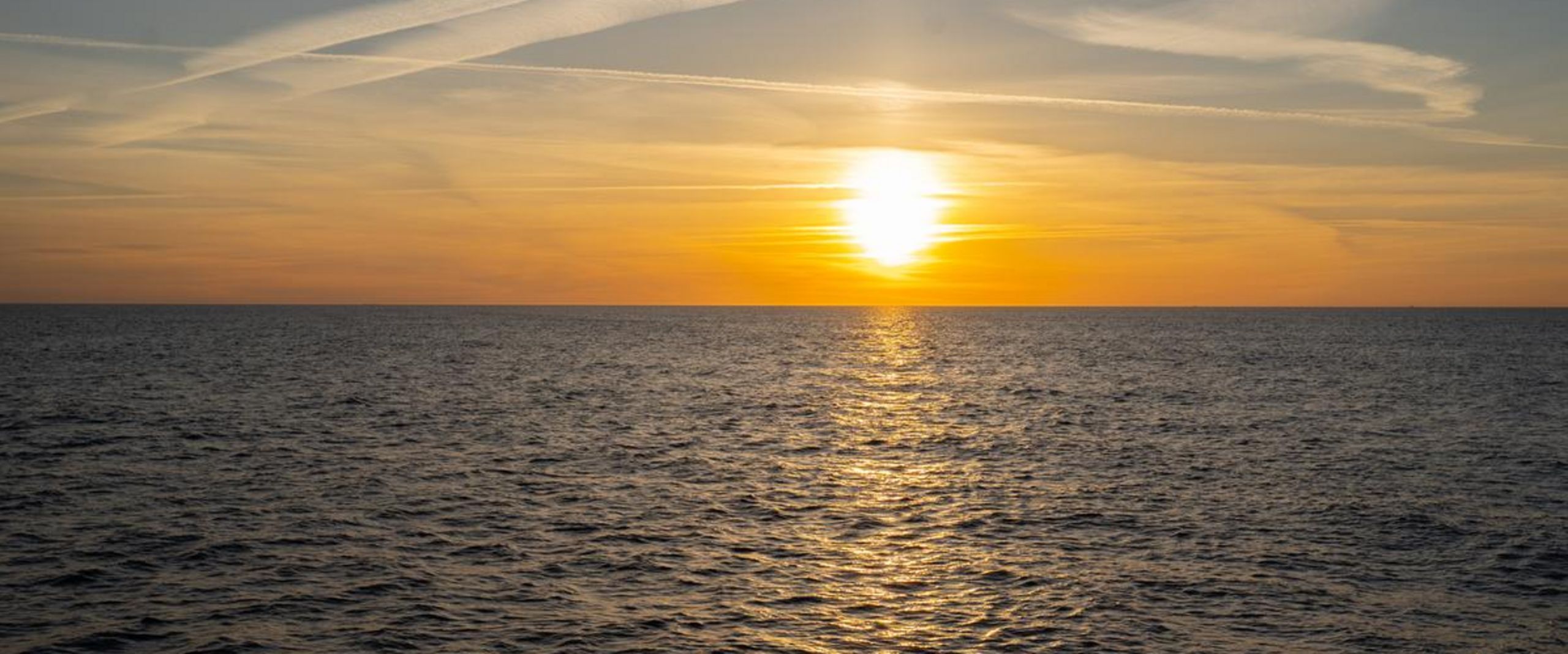 Nordsee Sonne Sonne steht hinter einem gelben Himmel über dem Horizont. Im Vordergrund ist das Meer zu sehen.