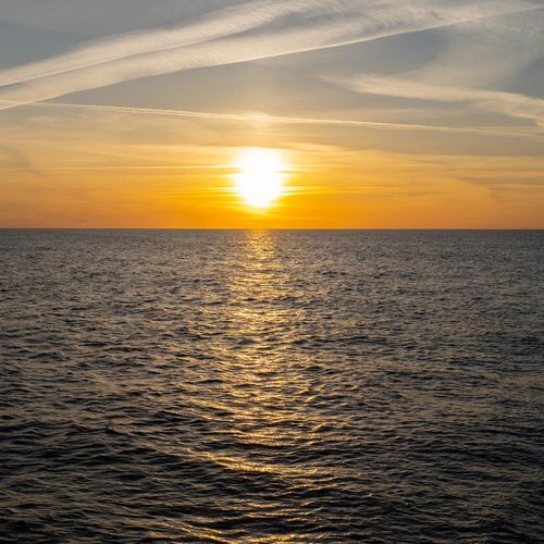 Sonne steht hinter einem gelben Himmel &uuml;ber dem Horizont. Im Vordergrund ist das Meer zu sehen.