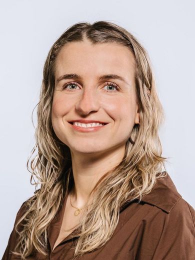 Auf dem Bild ist Janina Ebner zusehen. Sie hat langes blondes Haar und trägt eine braune Bluse. 