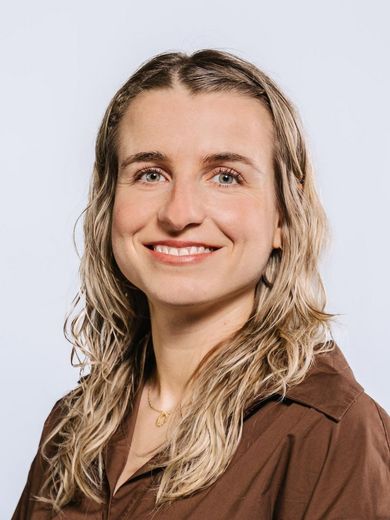Auf dem Bild ist Janina Ebner zusehen. Sie hat langes blondes Haar und trägt eine braune Bluse. 