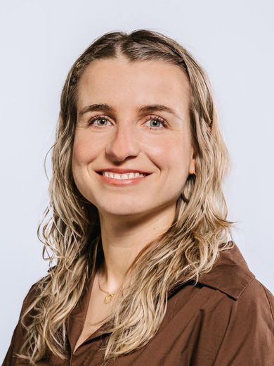 Auf dem Bild ist Janina Ebner zusehen. Sie hat langes blondes Haar und trägt eine braune Bluse. 