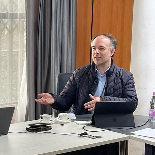 Zwie M&auml;nner am Tisch. einer redet, der andere schaut ins Laptop.