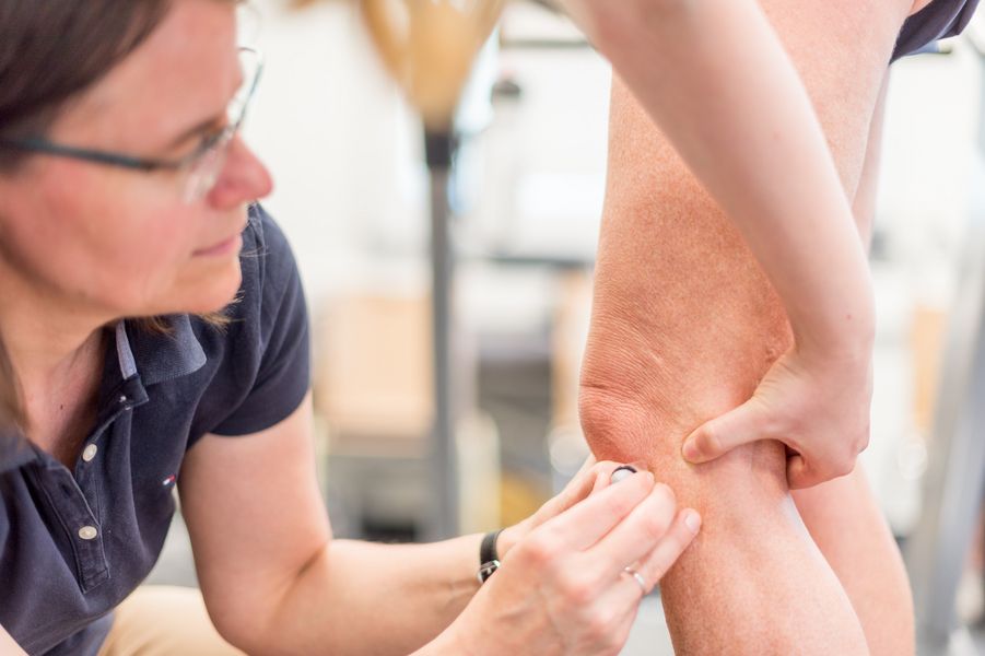 Übung Physiotherapie Eine Frau bringt einen Sensor am Knie einer Studentin an, um damit Bewegungen aufzuzeichnen.