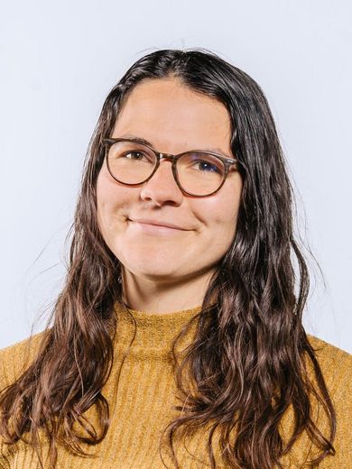 Auf dem Bild ist Hannah Graute zusehen. Sie hat lange braune Haare. Sie trägt eine Brille und einen Senffarbenden Pullover. 