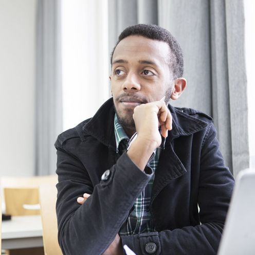 Ein Student sitzt nachdenklich vor einem Laptop in einem Seminarraum.