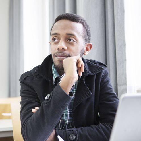 Ein Student sitzt nachdenklich vor einem Laptop in einem Seminarraum.