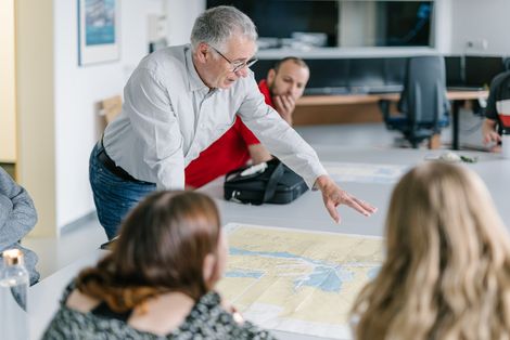 Professor Jung und Nautikstudierende arbeiten mit einer Seekarte.