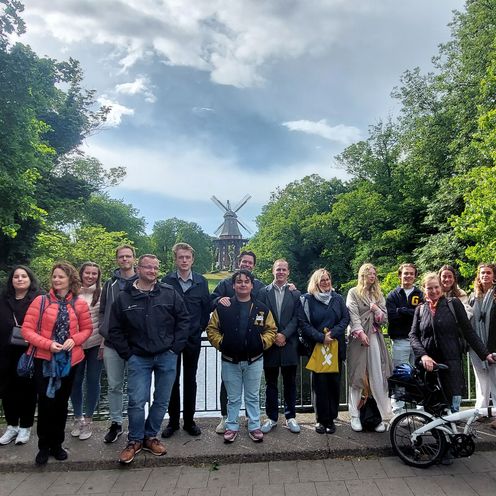 Studierendengruppe steht vor malerischer Kulisse mit Gr&uuml;nfl&auml;che und M&uuml;hle im Hintergrund
