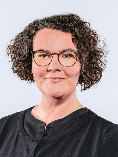 Auf dem Foto ist Johanna Brauns zusehen. Sie hat kurze lockiges Haar und trägt eine Brille. Sie hat ein schwarzes Oberteil an. 