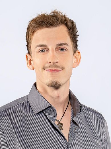 Auf dem Foto ist Jannik Schulz zusehen. Er hat kurze blonde Haare und einen Schn&auml;uzer, sowie einen Kinnbart. Er tr&auml;gt ein graues Hemd.