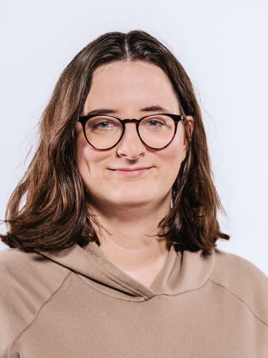 Auf dem Bild ist Jaqueline Stüve zu sehen. Sie hat schulterlanges braunes Haar. Sie trägt eine runde Brille und einen braunen Hoodie. 