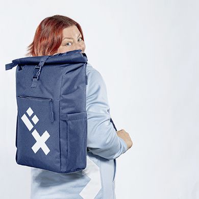 Eine Studentin schaut &uuml;ber ihre Schulter nach hinten zur Kamera. Sie tr&auml;gt einen dunkelblauen Rucksack mit HSB-Logo.