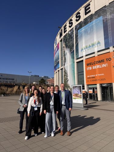 Das Foto zeigt eine Gruppe an Studierenden und Professoren, die vor dem Messegel&auml;nde in Berlin stehen. Die Sonne scheint. 