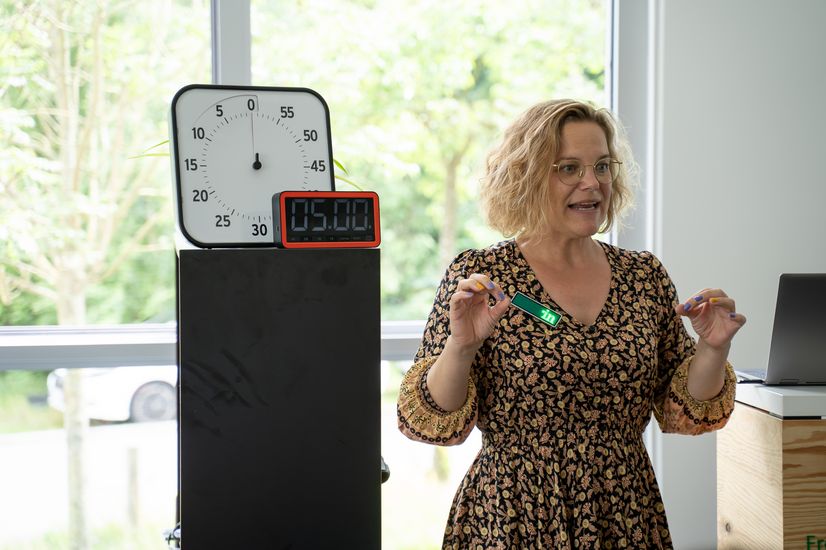 Auf dem Bild ist eine blonde Frau neben einer digitalen Stoppuhr zusehen. Die Uhr zeigt 5 Minuten an. 
