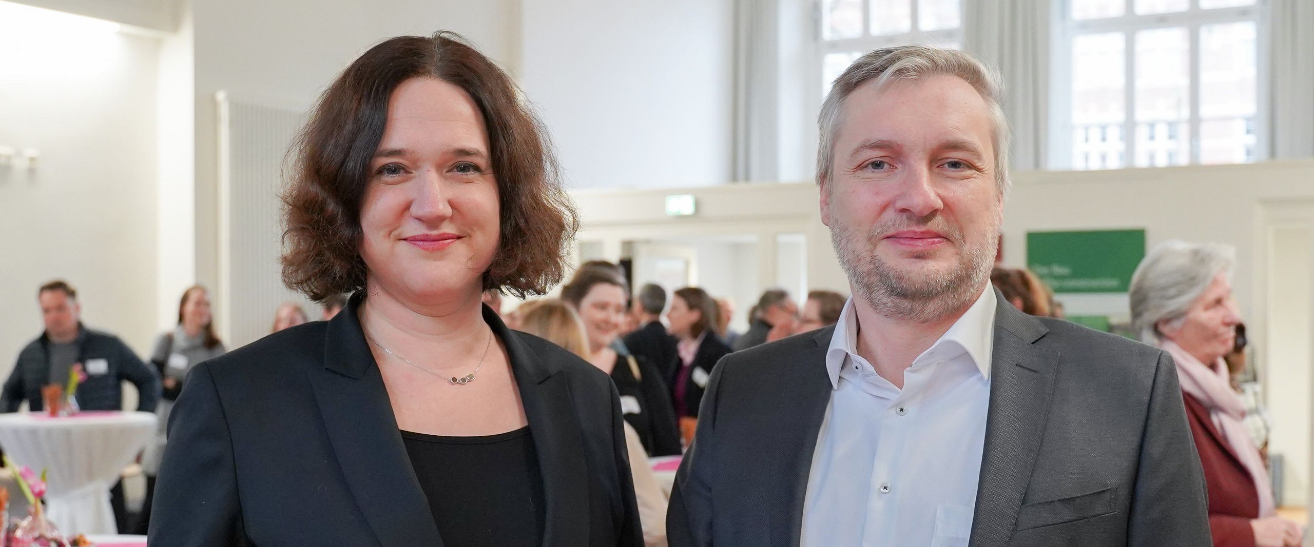 Bild von Frau und Mann an Stehtisch. Beide lächeln in die Kamera.