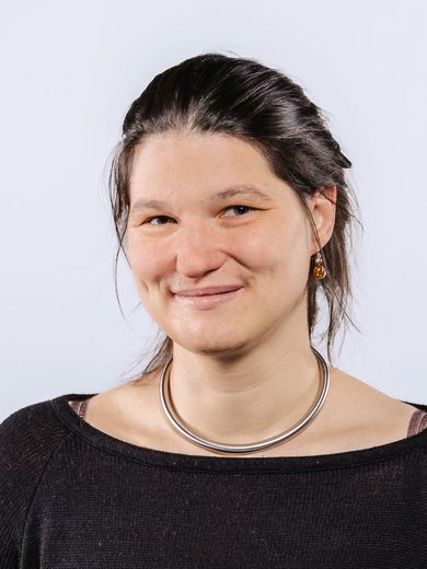 Auf dem Bild ist Wiebke Ebbt Lindheimer zusehen. Sie hat ihre langen braunen Haare zu einem tiefen Dutt zusammengebunden. Sie trägt einen dunkelgrauen Pullover und eine Halskette. 