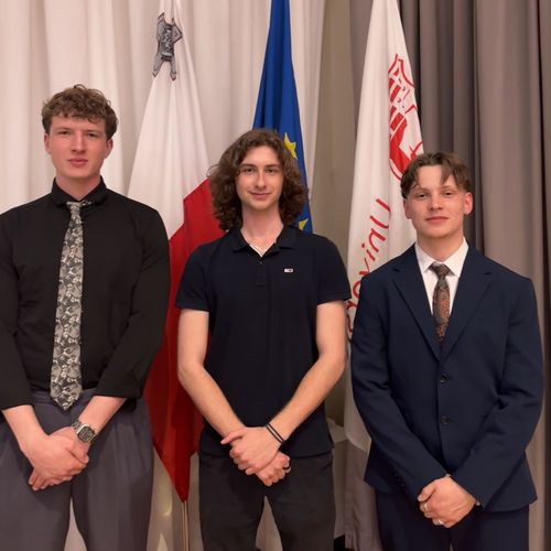 A group photo of three young men. They are standing in front of flags.