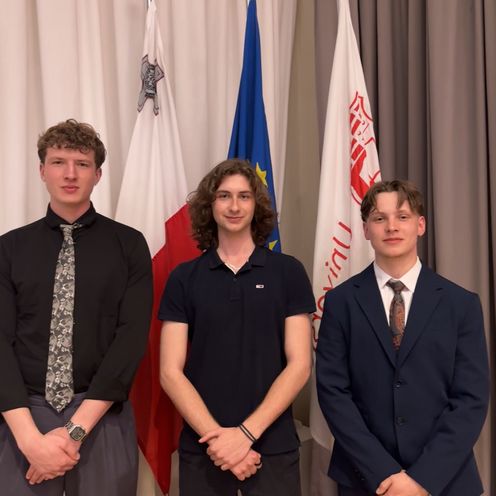 Gruppenbild mit drei jungen M&auml;nnern. Sie stehen vor Fahnen.
