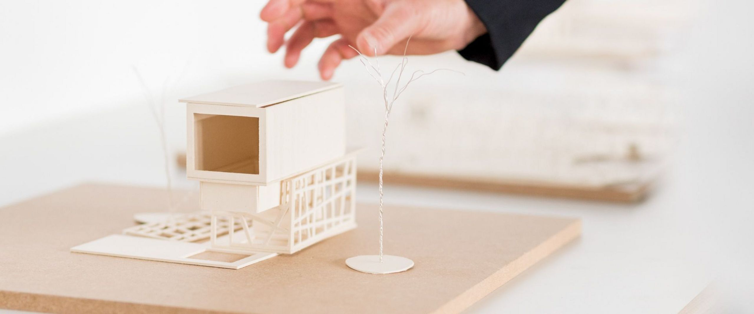 Eine Hand greift nach einem Modell eines Hauses. 