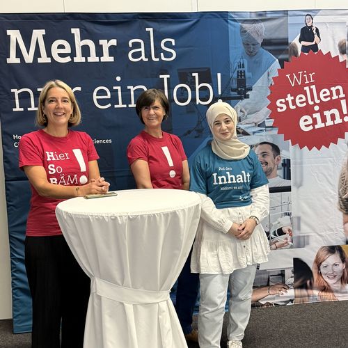 Ggruppenfoto mit drei Frauen an einem Stehtisch vor einem gro&szlig;en Banner