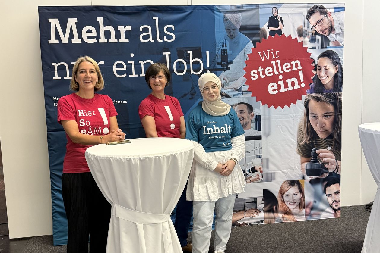 Ggruppenfoto mit drei Frauen an einem Stehtisch vor einem gro&szlig;en Banner