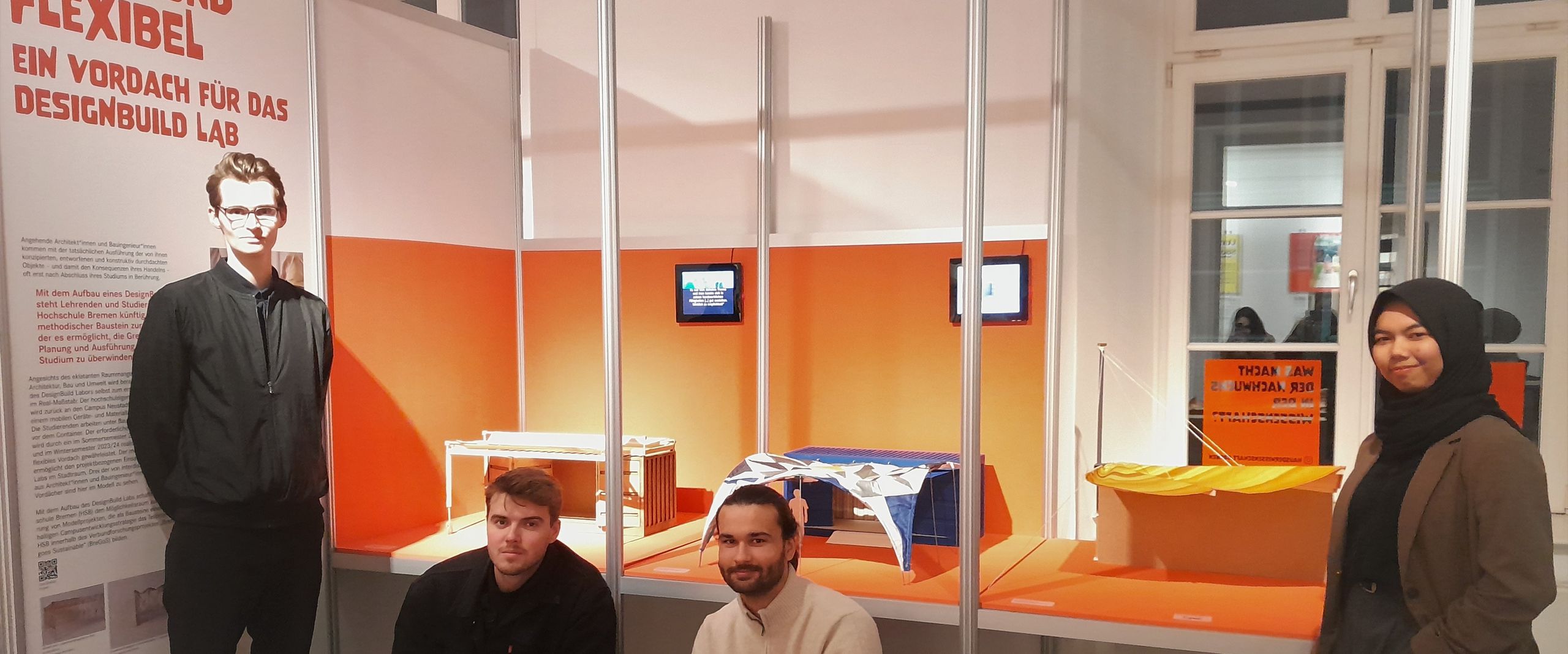 Drei Männer und eine Frau vor Architekturmodellen