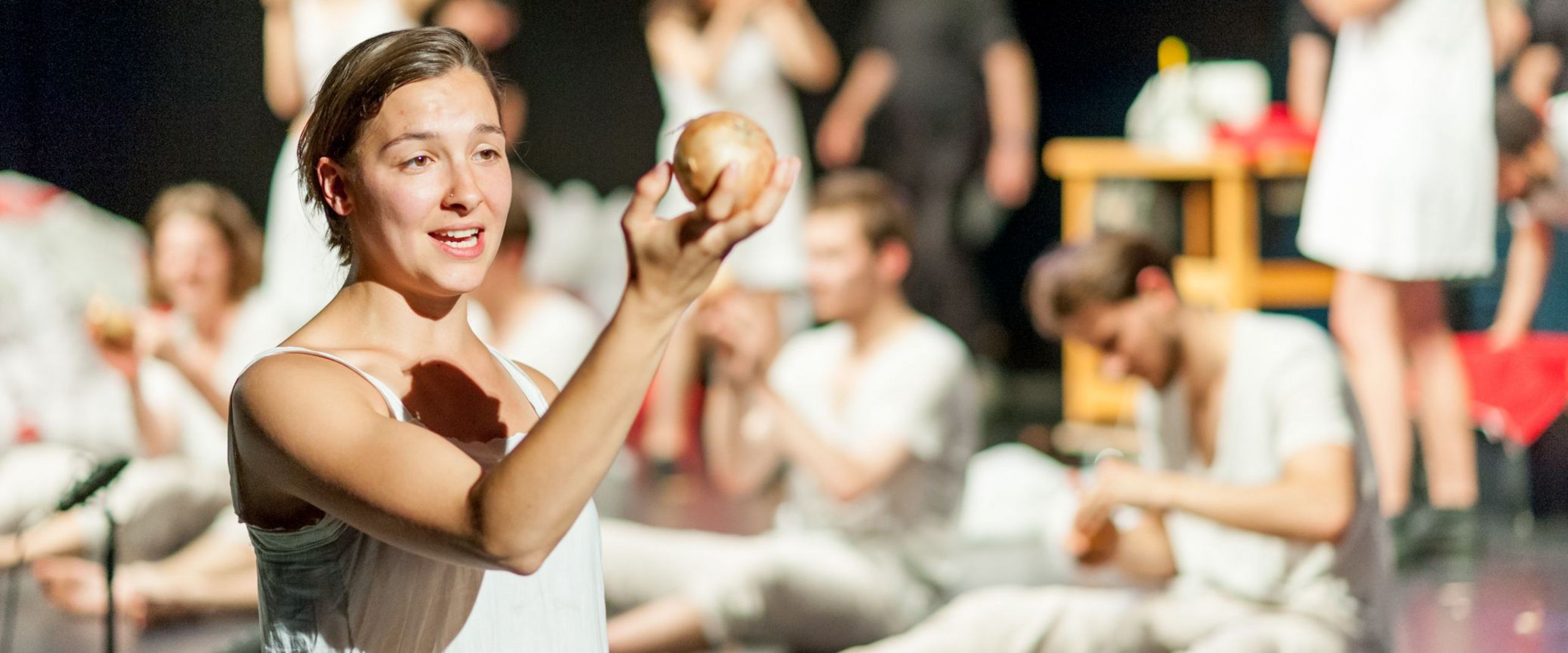 Bühnenszene aus dem Theaterstück "Peer Gynt". Im Vordergrund steht eine junge Frau, die eine Kugel hochhält.