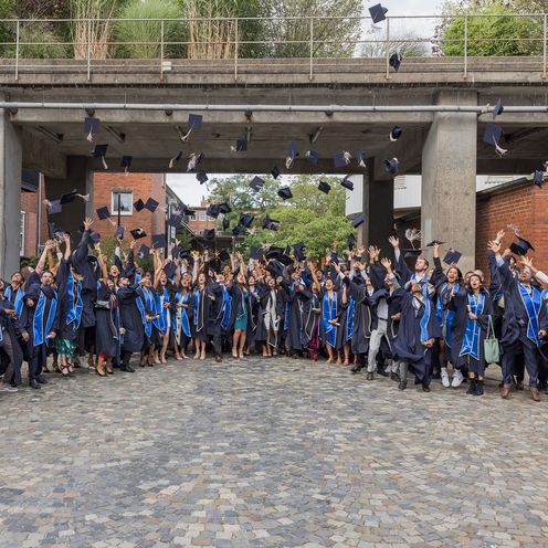 Graduiertenfeier: Menschen stehen in einer Gruppe zusammen und werfen ihre H&uuml;te hoch und lachen.
