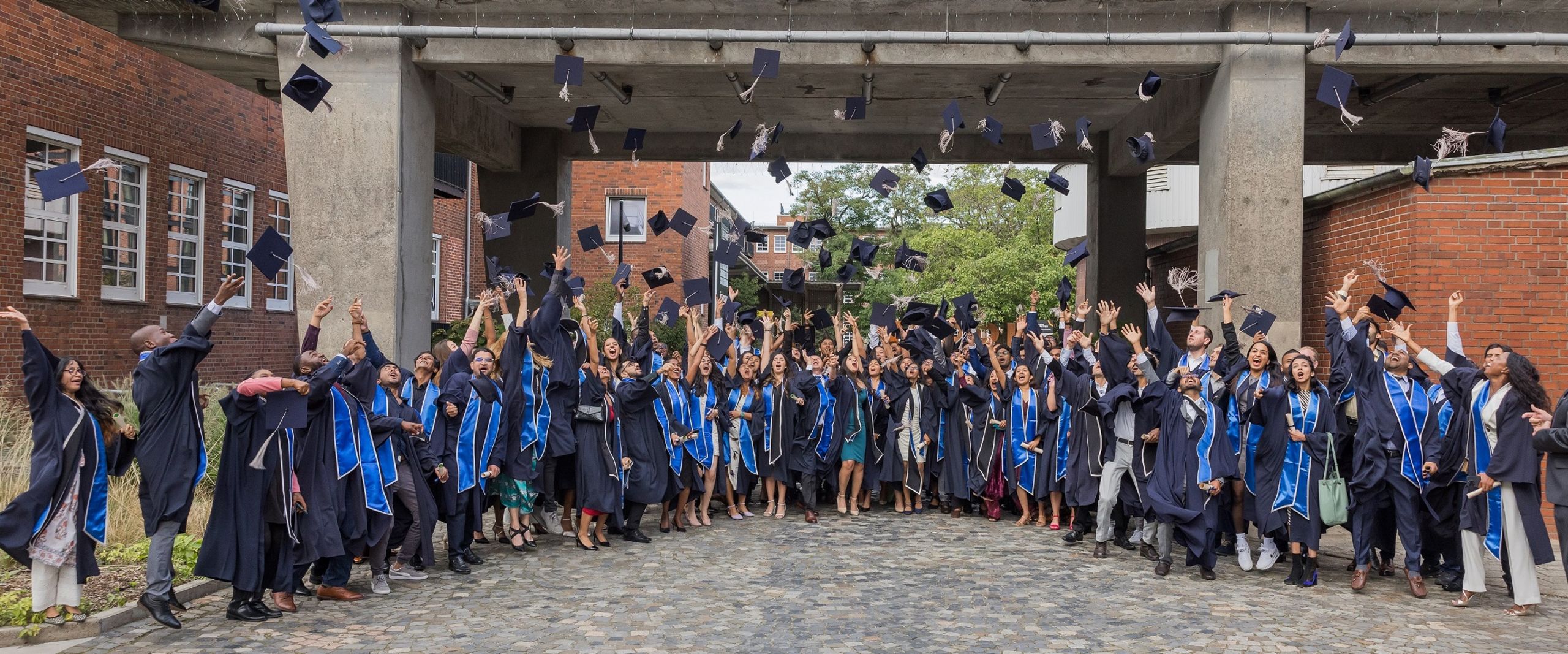 Graduiertenfeier: Menschen stehen in einer Gruppe zusammen und werfen ihre H&uuml;te hoch und lachen.