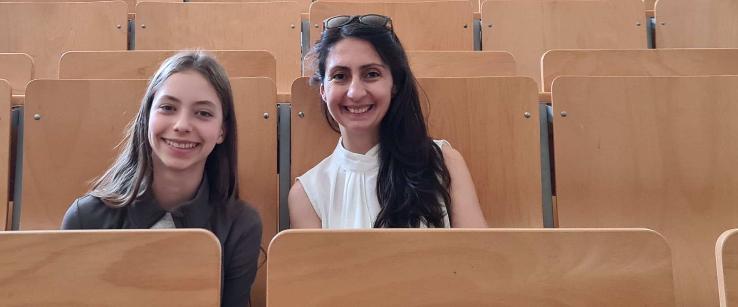 CyberMentor 2025 Colmorn Mädchen und junge Frau sitzen nebeneinander in einem Hörsaal und lachen in die Kamera