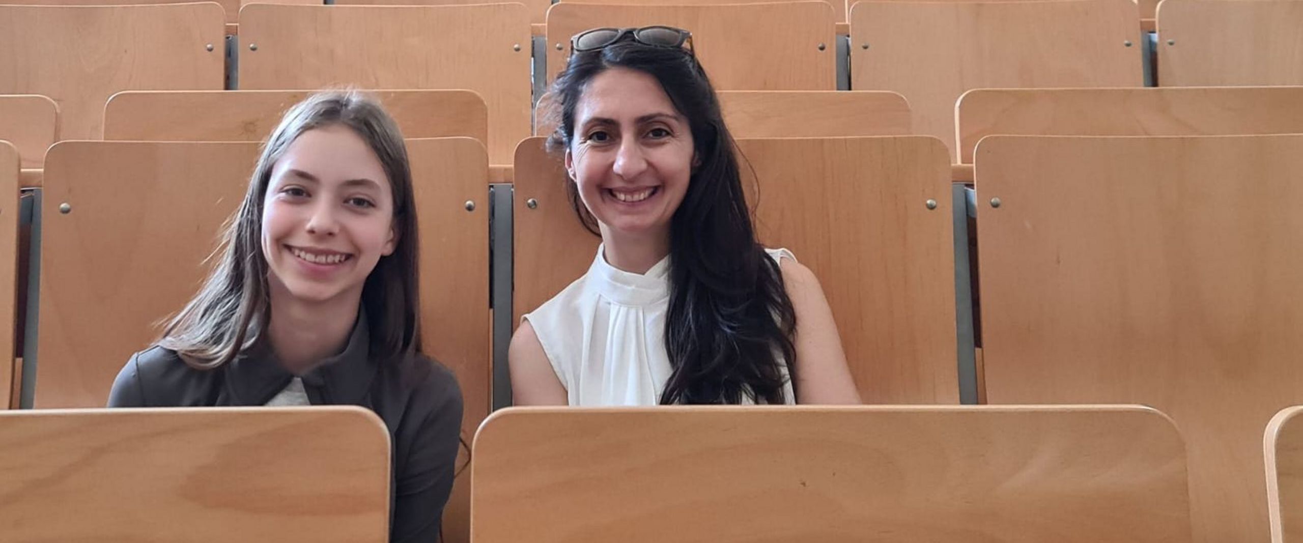CyberMentor 2025 Colmorn Mädchen und junge Frau sitzen nebeneinander in einem Hörsaal und lachen in die Kamera