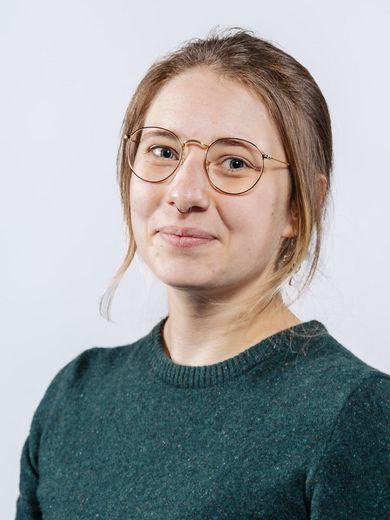 Auf dem Bild ist Maria von Einem zu sehen. Sie trägt ihr braunes Haar locker zusammengebunden, eine Brille und einen dunkelgrünen Pullover. 