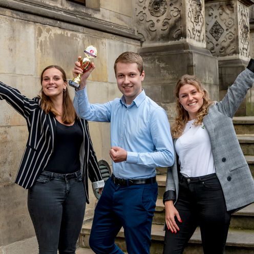 3 junge Gr&uuml;nder:innen jubelnd mit Pokal vor Sch&uuml;tting