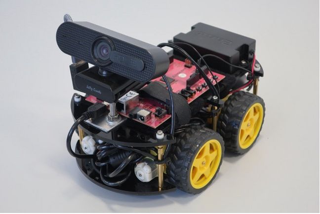 Robotisches Fahrzeug mit Bilderkennung auf einem raumfahrttauglichen FPGA Auf dem Bild ist ein Modellfahrzeug mit vier Rädern und einer kleinen Webcam abgebildet. Es steht vor einem weißen Hintergrund.
