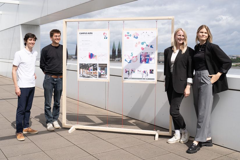 Junge M&auml;nner rund Frauen stehen neben Plakaten und lachen in die Kamera.