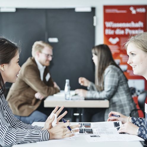 M&auml;nner und Frauen sitzen zu zweit an einem Tisch gegen&uuml;ber und unterhalten sich.
