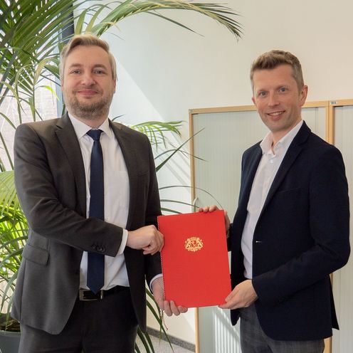 Zwei M&auml;nner l&auml;cheln in die Kamera und halten gemeinsam eine Urkunde