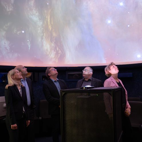 Drei M&auml;nner und zwei Frauen blicken im Dunkeln in den Sternenhimmel in einem Planetarium.
