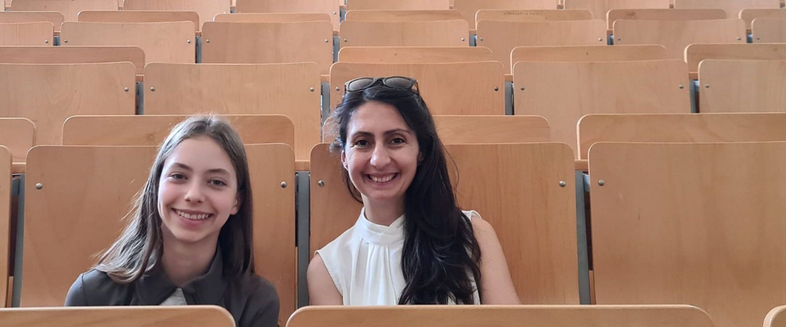 Mädchen und Frau Sitzen auf Stühlen nebeneinander in einem Hörsaal und lachen in die Kamera