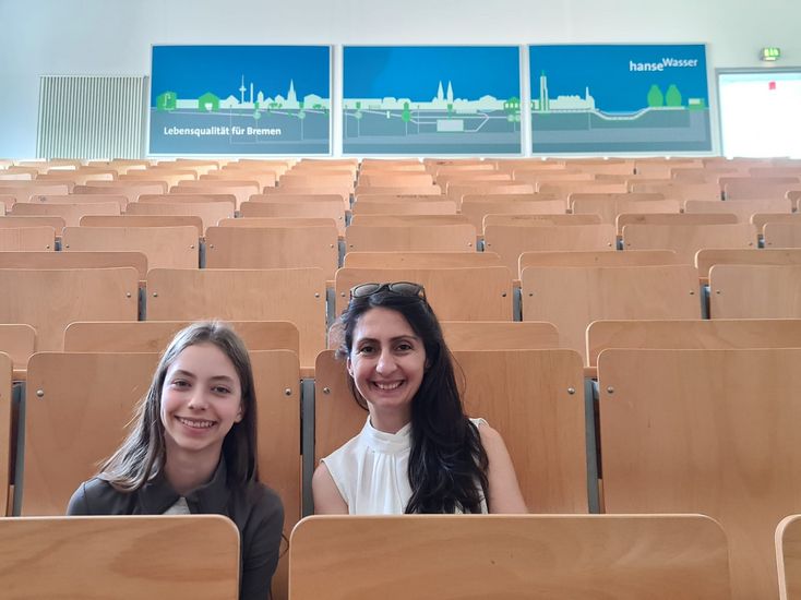 Mädchen und Frau Sitzen auf Stühlen nebeneinander in einem Hörsaal und lachen in die Kamera